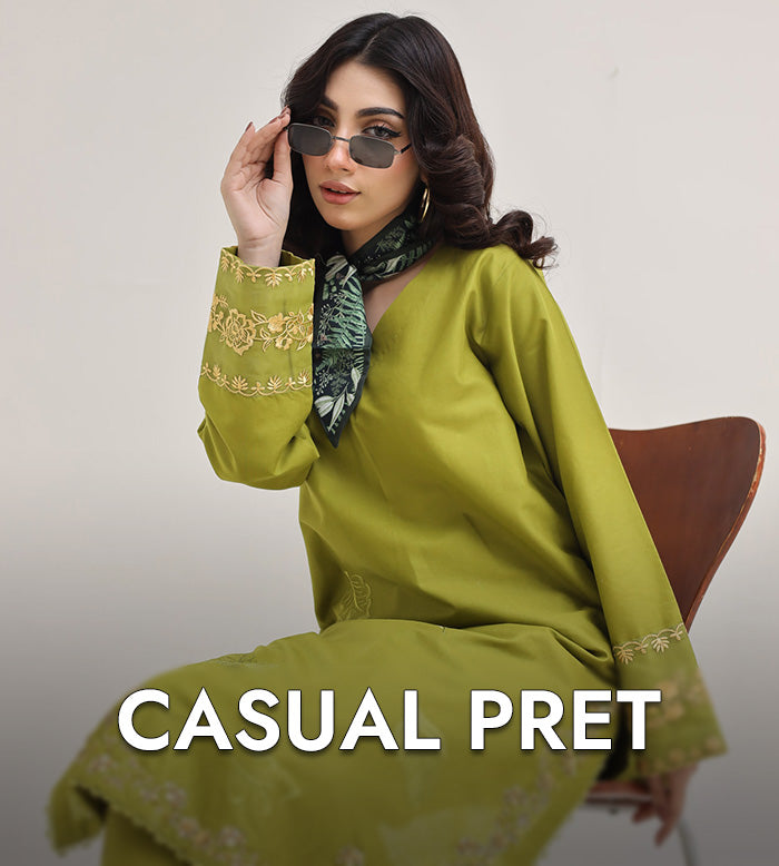 Woman wearing a green outfit with embroidery, sitting on a chair against a plain background.