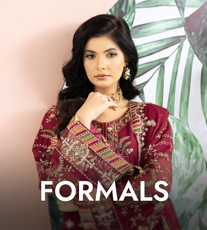 Woman wearing a maroon formal outfit with intricate designs, standing against a light background with green leafy elements.