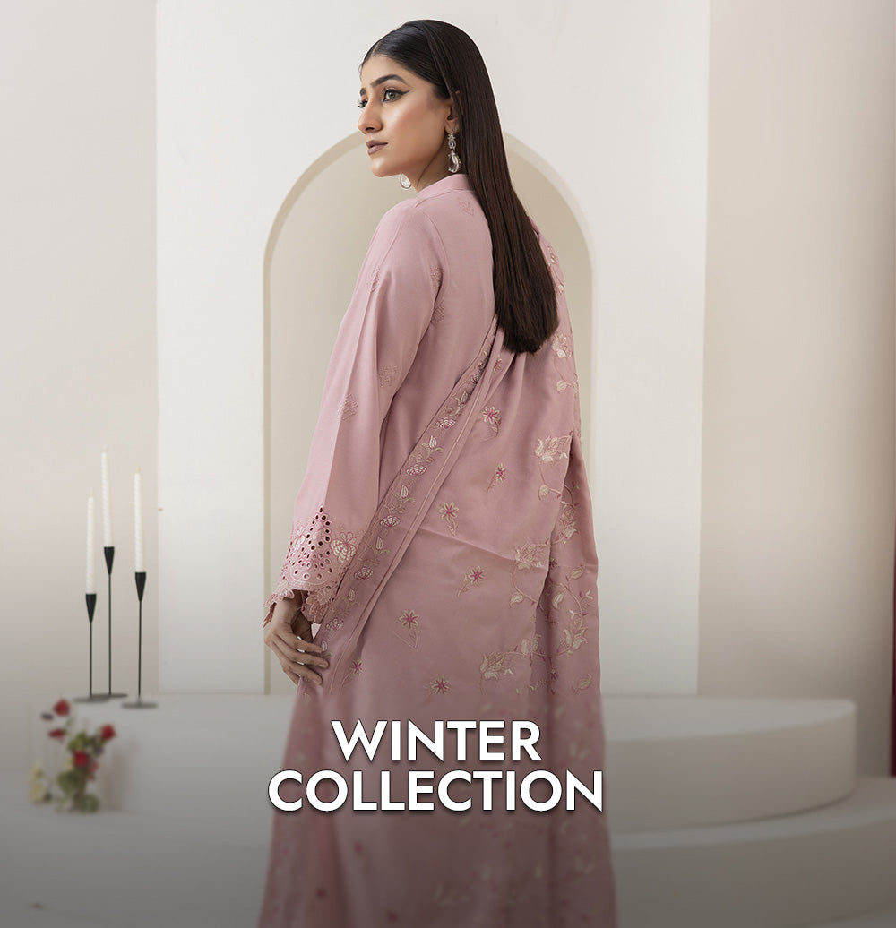 Woman wearing a pink saree with intricate designs, standing in a softly lit room with 'Winter Collection' text.
